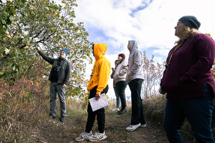 杰森圣. Saveur(最右边), 泉溪草原奥杜邦中心的高级教育经理, 指着中心小径上的一棵树. 三名澳门威尼斯人网址的学生和图书管理员卡利·比亚吉(Cali Biaggi)听着. 