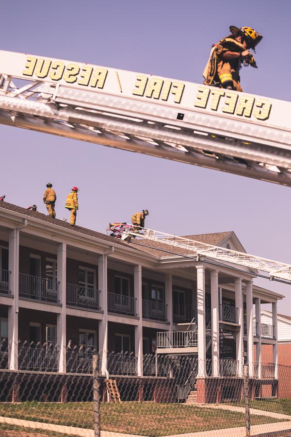 克里特岛志愿消防部门的一辆卡车的梯子上，一名消防员从伯拉格大厅的屋顶下来. 其他消防员正在练习在宿舍楼屋顶切割通风口, 今年夏天晚些时候将被拆除. 